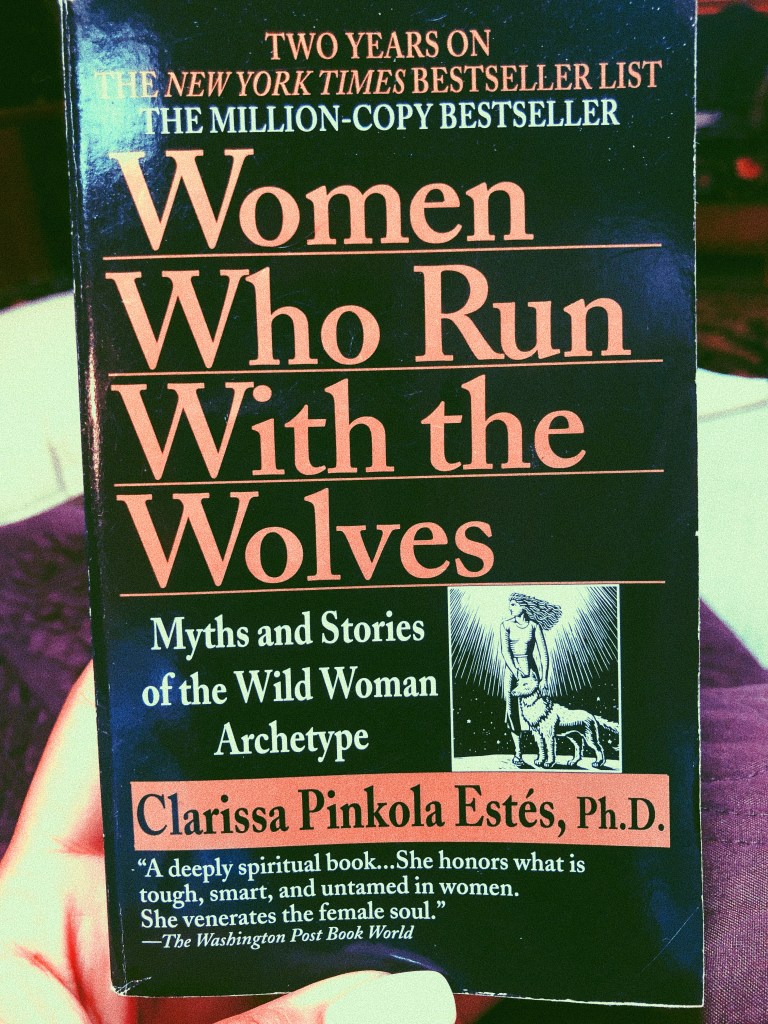 image of hand with acrylic nails holding up the book "women who run with the wolves" by clarissa pinkola estes, ph.d.